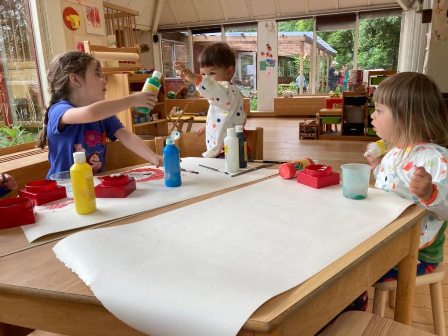 Drie peuters op democratische school De Ruimte zitten rond een tafel en zijn bezig met een groot vel papier te beschilderen.