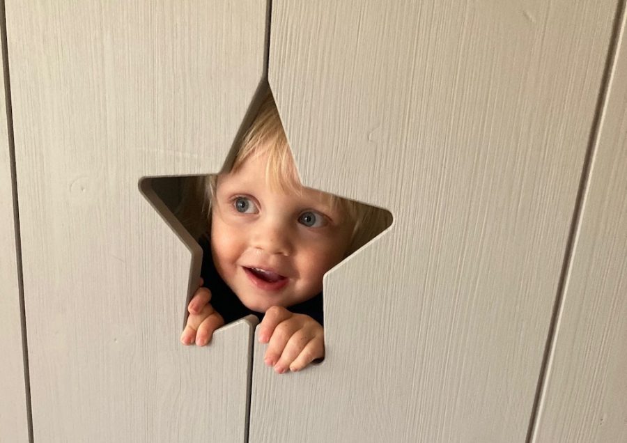 een blij gezichtje kijkt door een stervormig gat in een deurtje