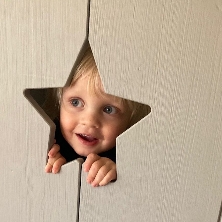 een blij gezichtje kijkt door een stervormig gat in een deurtje