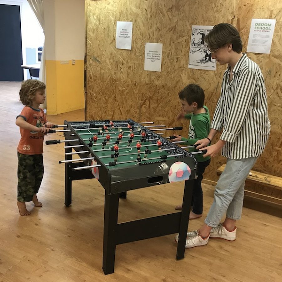 Twee jonge leerlingen en een oudere spelen samen tafelvoetbal.