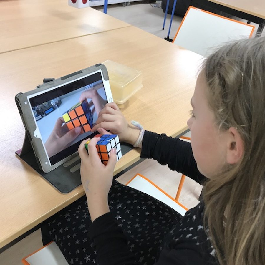a pupil watches a tutorial on Rubiks Cube. She holds one in her hand.