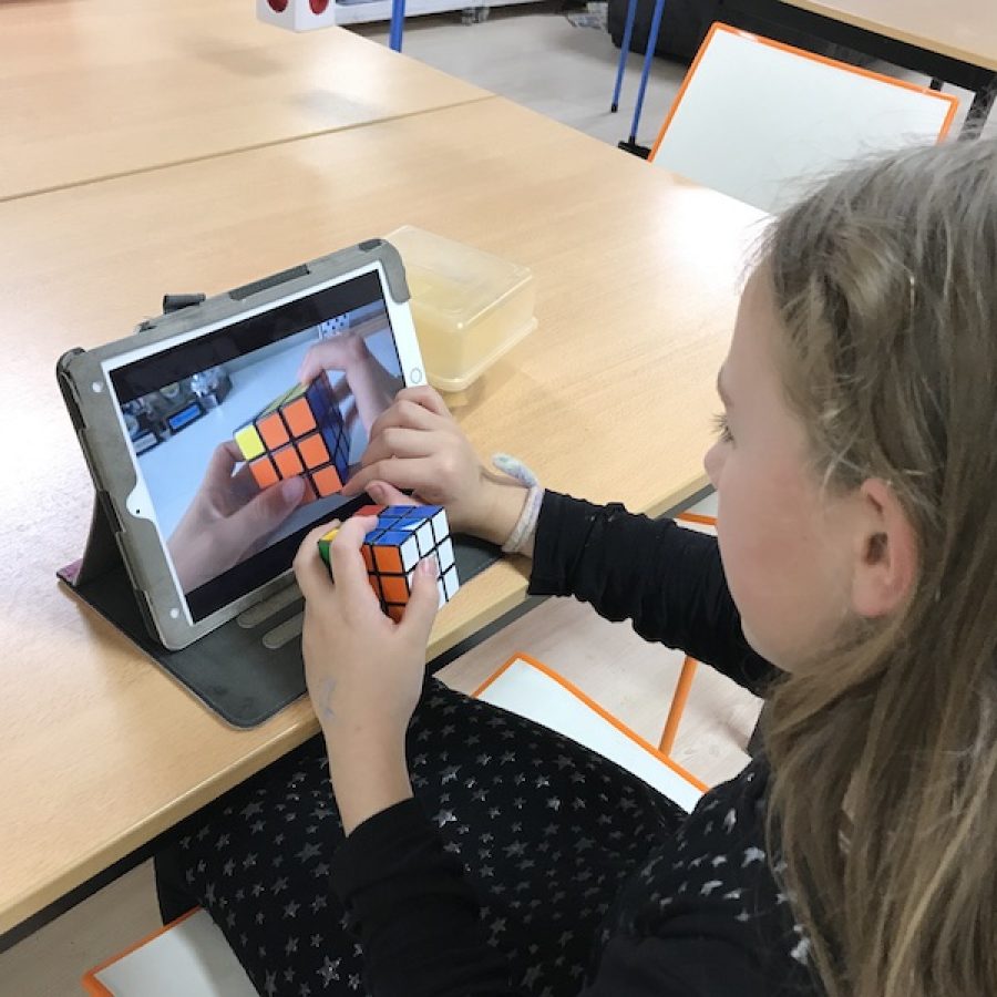 een student kijkt op een scherm waarop een Rubik's kubus te zien is. Zelf heeft ze er een in haar hand.