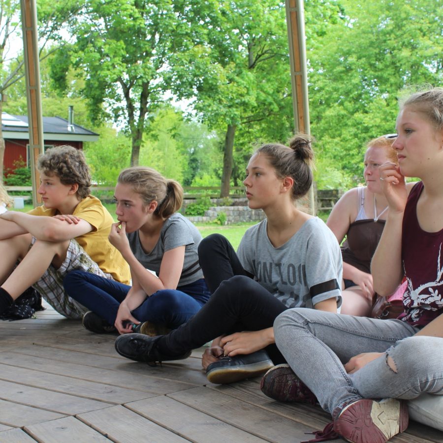 Studenten van De Ruimte zitten op een houten vloer te luisteren.
