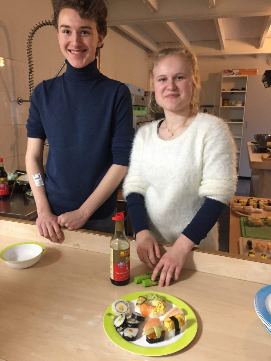 Fingal, student op De Ruimte, staat links. Rechts van hem staat Suzanne, ook student op De Ruimte. Voor hen op tafel staat sushi op een bordje. Ze kijken blij.