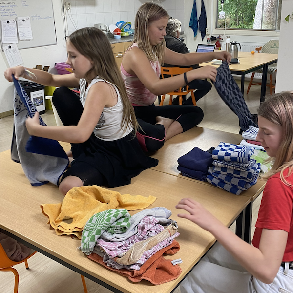 Sitting at and on a table three students are folding laundry