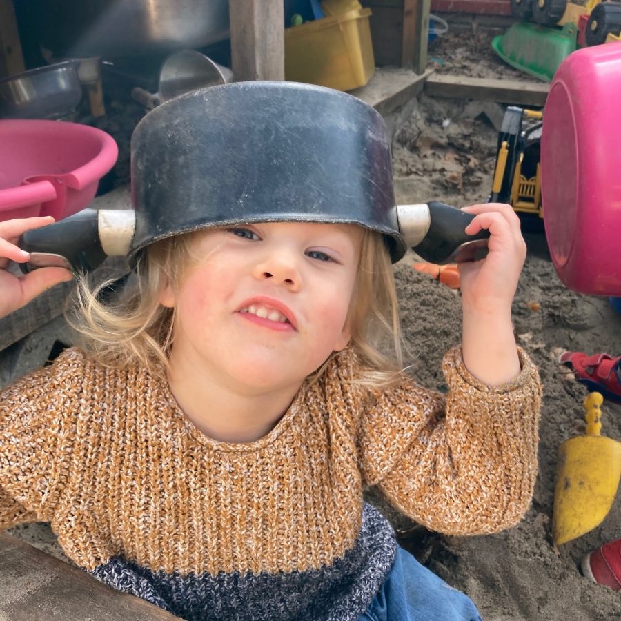 A toddler looks joyfull, he holds a pan on his head with both hands