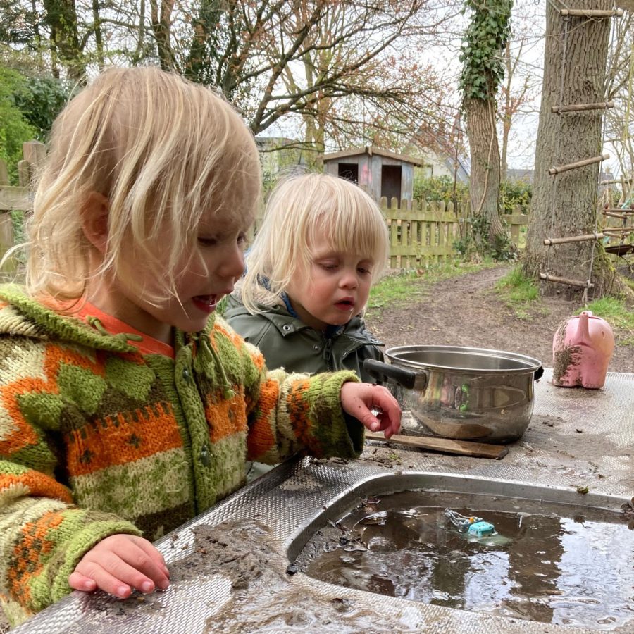 two toddlers are playing with water and sand outside