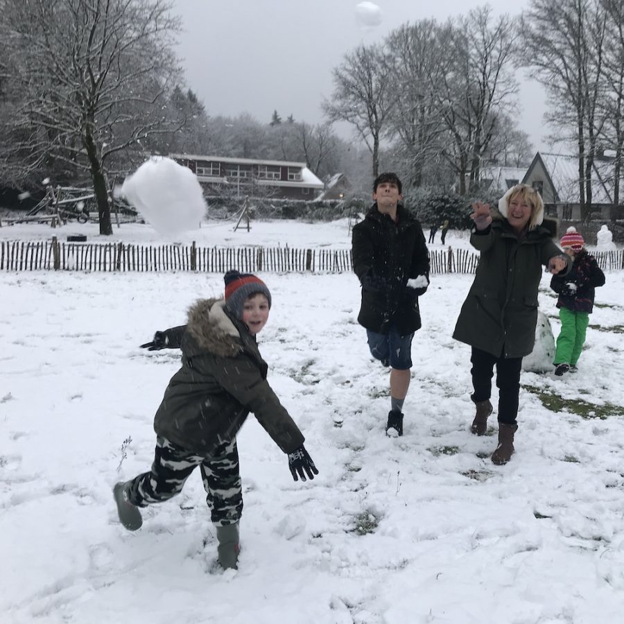 Een student gooit een sneeuwbal richting de camera, twee stafleden doen mee en lachen