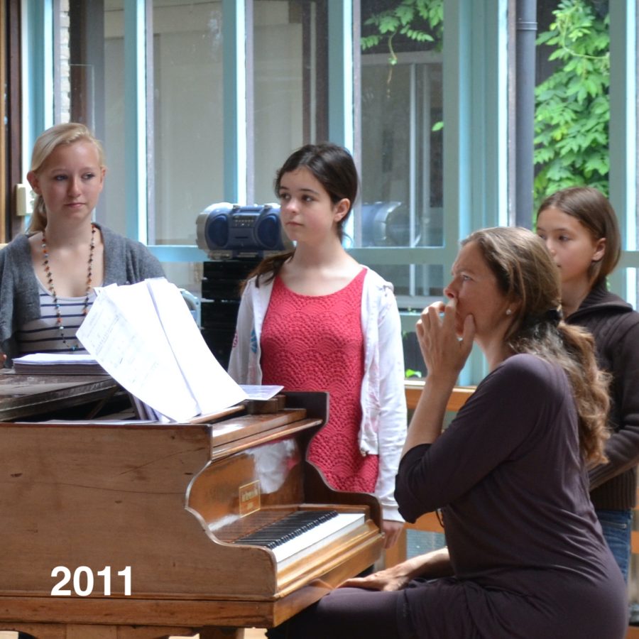 Zangdocent Meike van de Linden achter de piano, 3 studenten kijken toe, klaar om te gaan zingen.