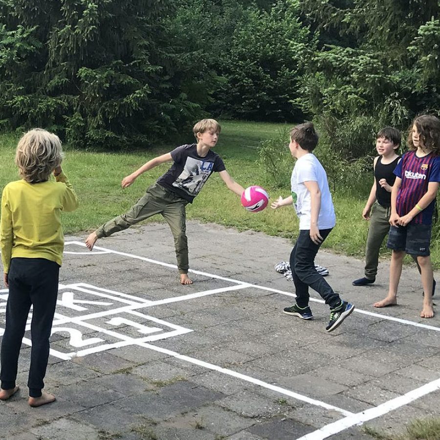 Vijf leerlingen staan buiten op een zogenaamd Kingen-veld, en spelen het spel Kingen. Een van hen heeft net een bal opgevangen in zijn hand.