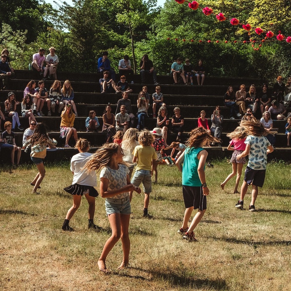 In het amfitheater van De Ruimte danst een groep jonge studenten in het gras. De haren zwieren.