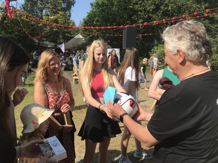 Studenten en stafleden van democratische scholen geven cadeaus aan staflid Ruud. Een van hen overhandigt een volleybal.