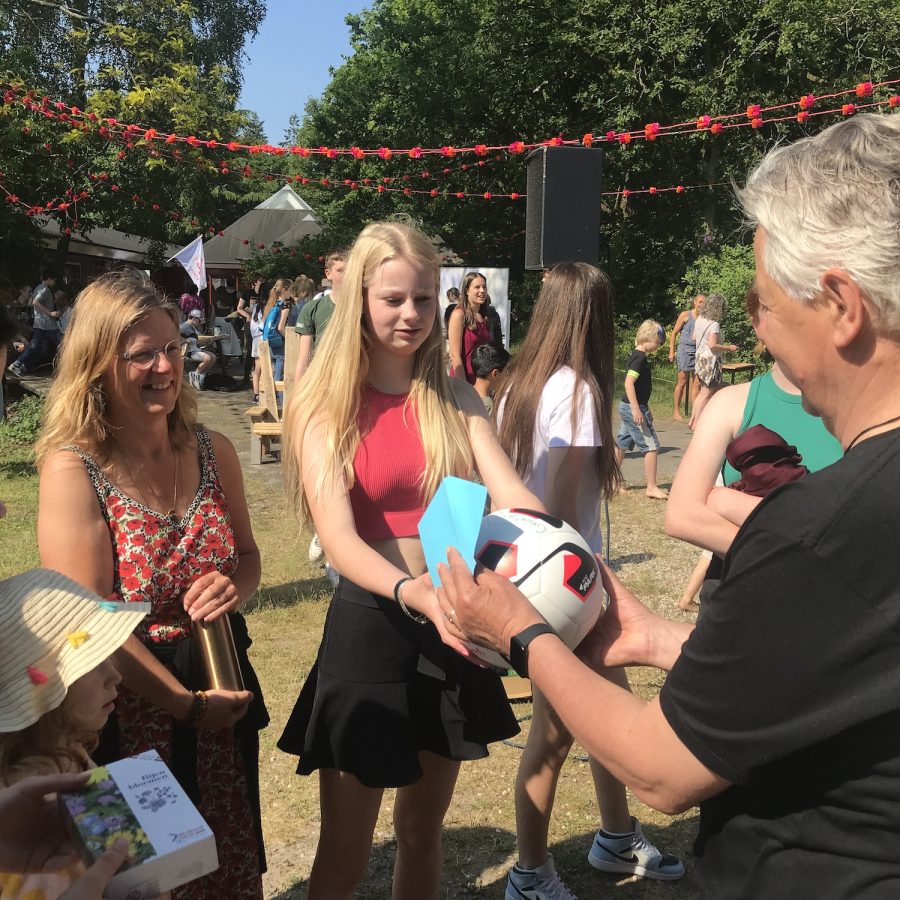 Studenten en stafleden van democratische scholen geven cadeaus aan staflid Ruud. Een van hen overhandigt een volleybal.