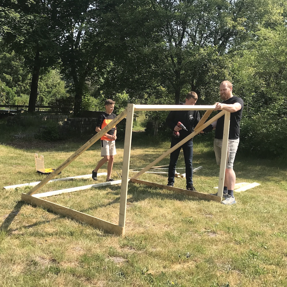 Studenten Kyano en Lucas bouwen samen met staflid Stern een houten voetbalgoal.