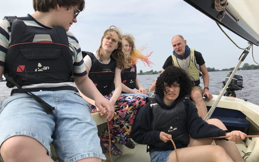 Vier studenten en een staflid in een zeilboot. Een van de studenten houdt een fokkeschoot in haar handen. Er is concentratie te zien op de gezichten.