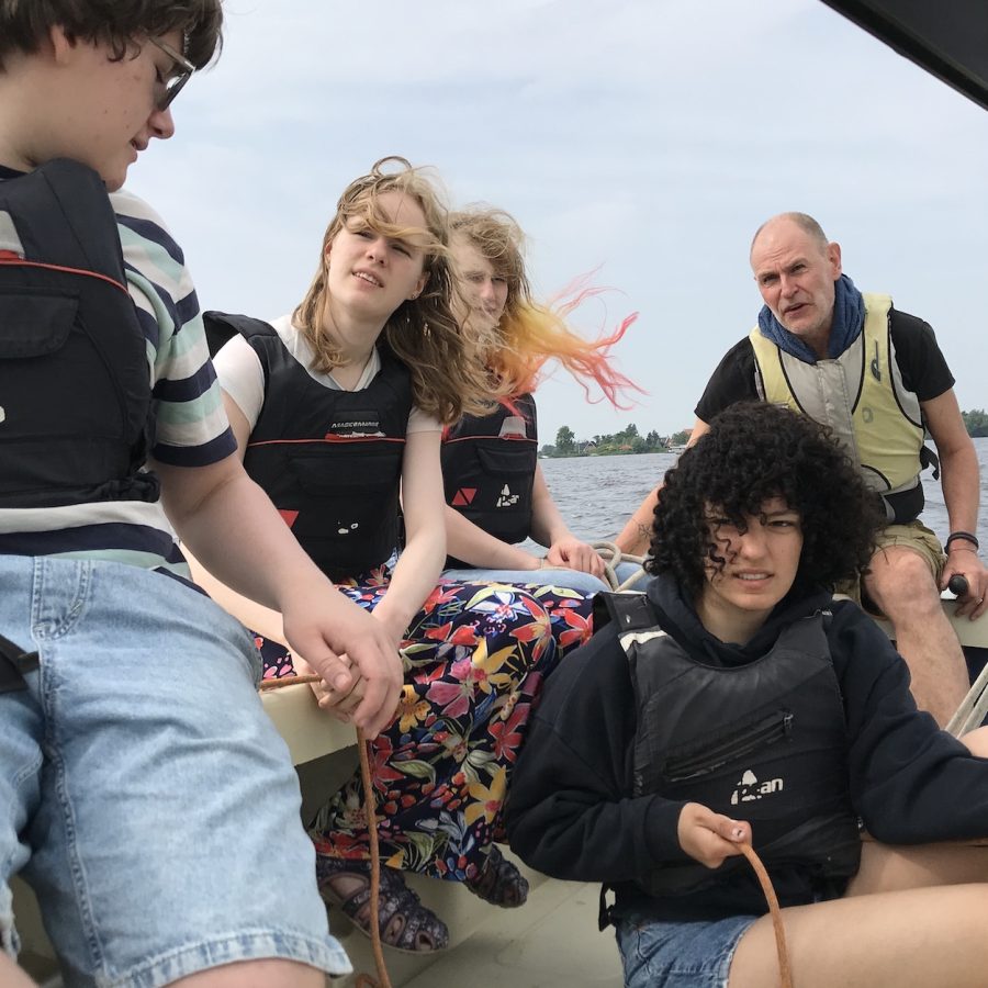 Vier studenten en een staflid in een zeilboot. Een van de studenten houdt een