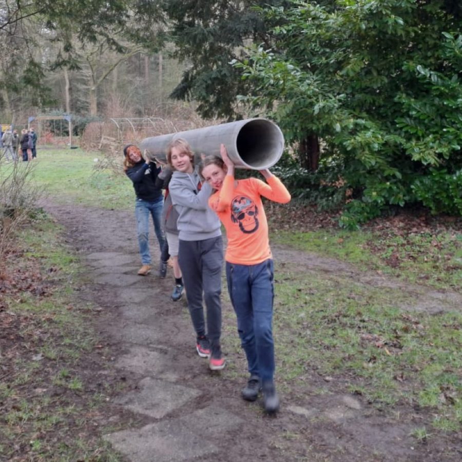 Vier studenten sjouwen een grote grijze plastic buis: een van de drijvers voor hun te bouwen zeilboot. Ze kijken trots en lachen.