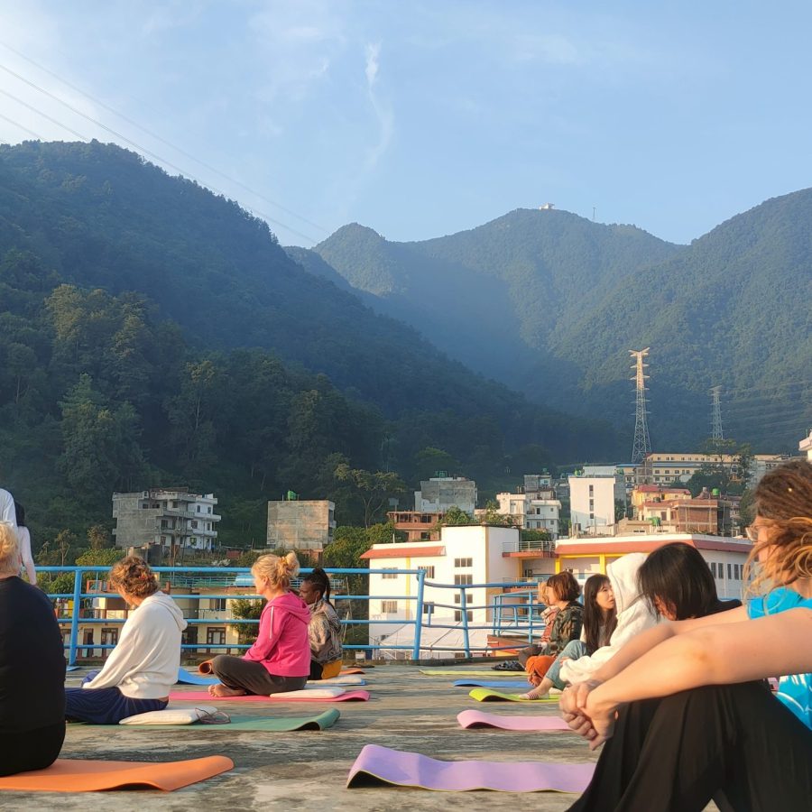 Deelnemers van IDEC Nepal zitten op matjes op het dak van een gebouw, met uitzicht op de bergen.