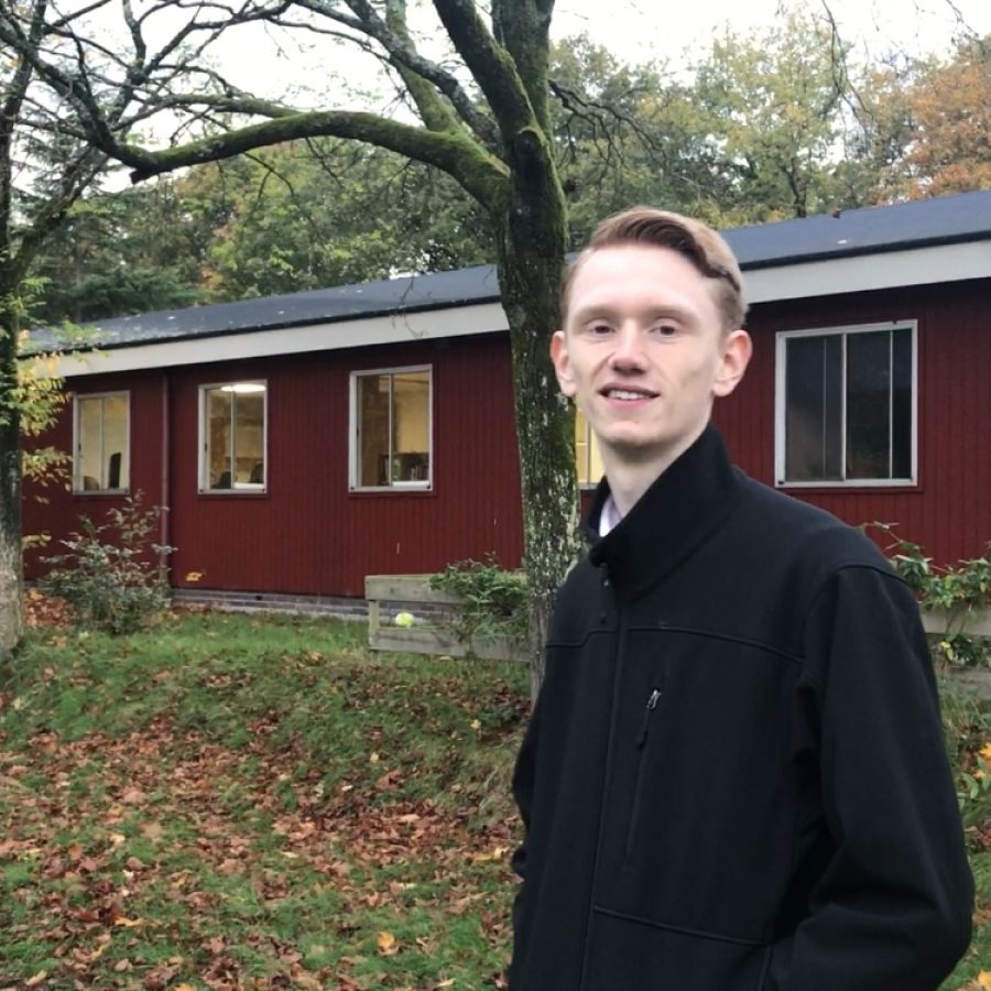 Oud-student Jasper staat buiten voor het roodgekleurde gebouw van De Ruimte. In een herfstige omgeving.