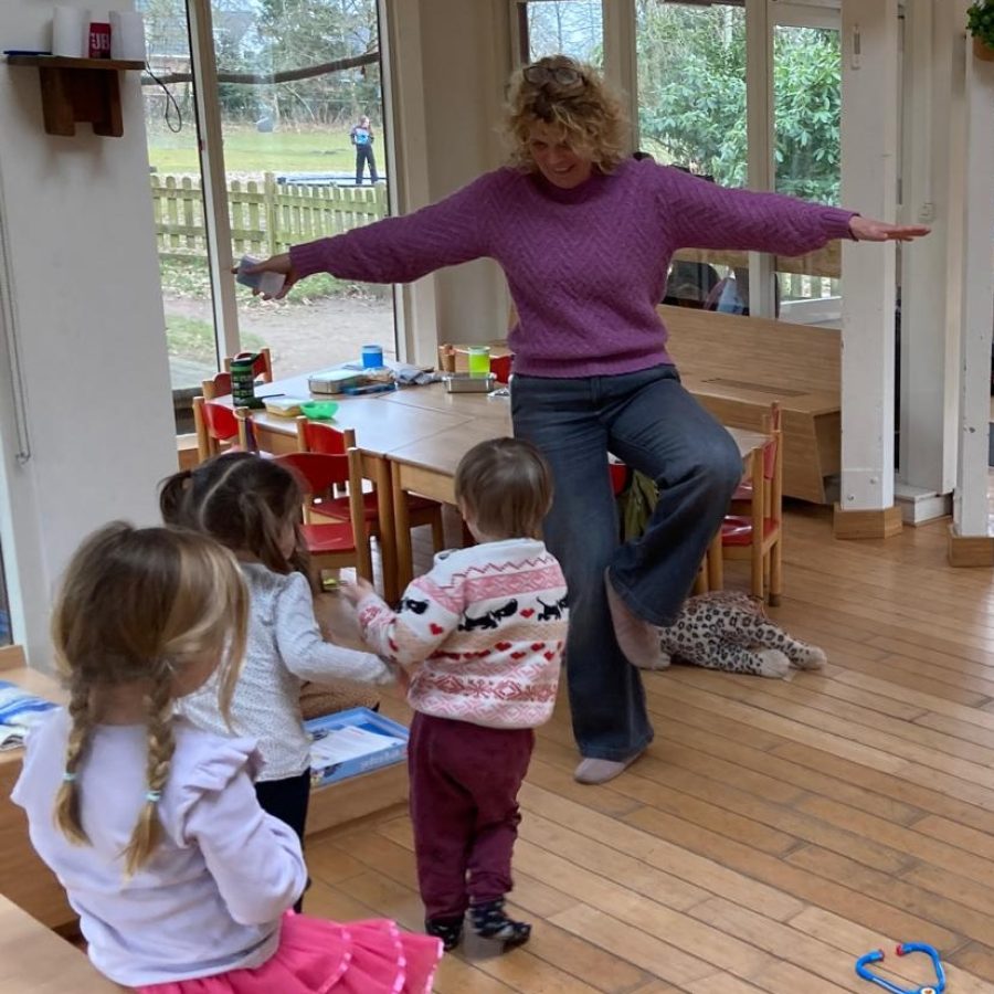 20250626_vacature-peuters Begeleider bij de peutergroep Jolanda staat in een yogapose, drie peuters kijken naar haar.